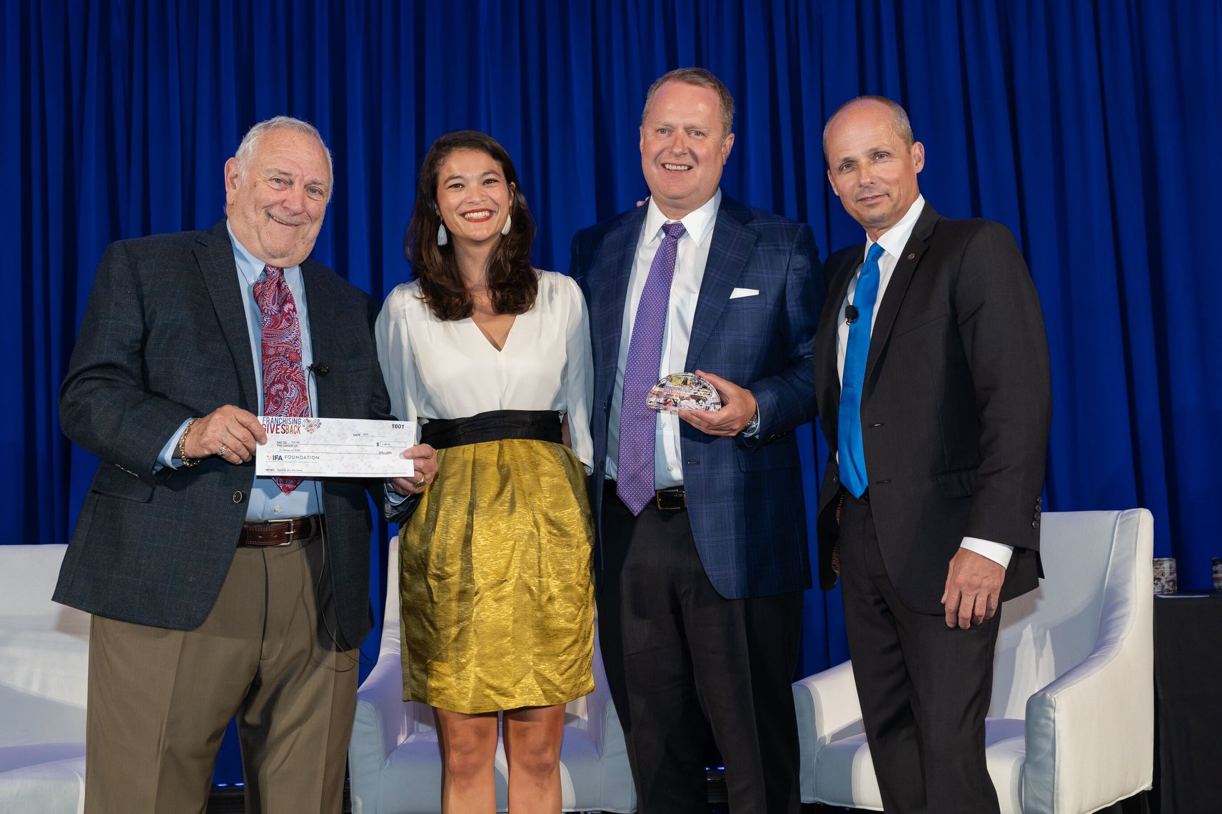 Four people stand together, with one man holding an award